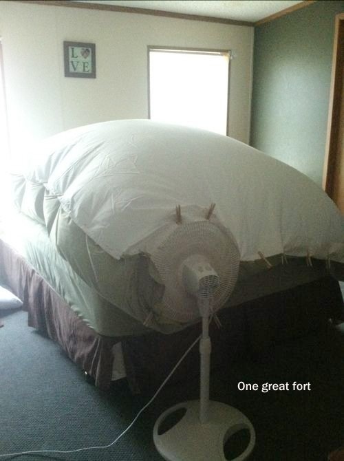 a bed with a fan on top of it in a room next to a window