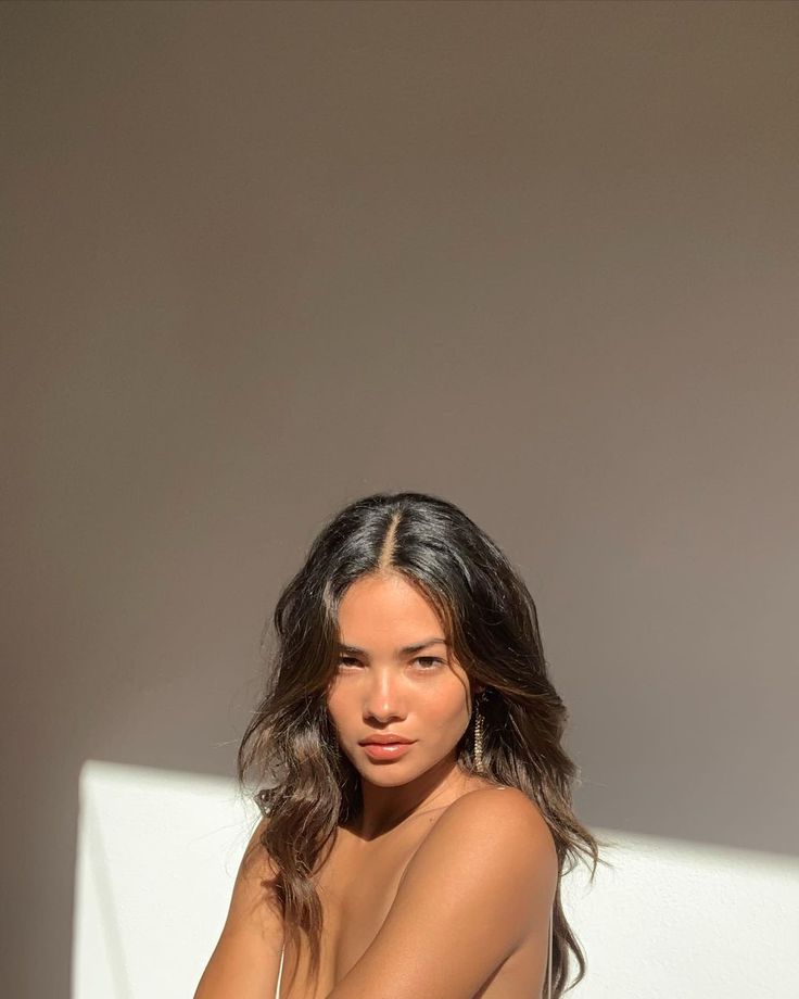 a woman sitting on top of a white chair next to a wall with her legs crossed