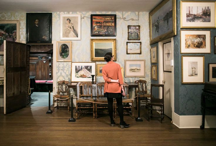 a woman standing in the middle of a room with many pictures on the wall and around her