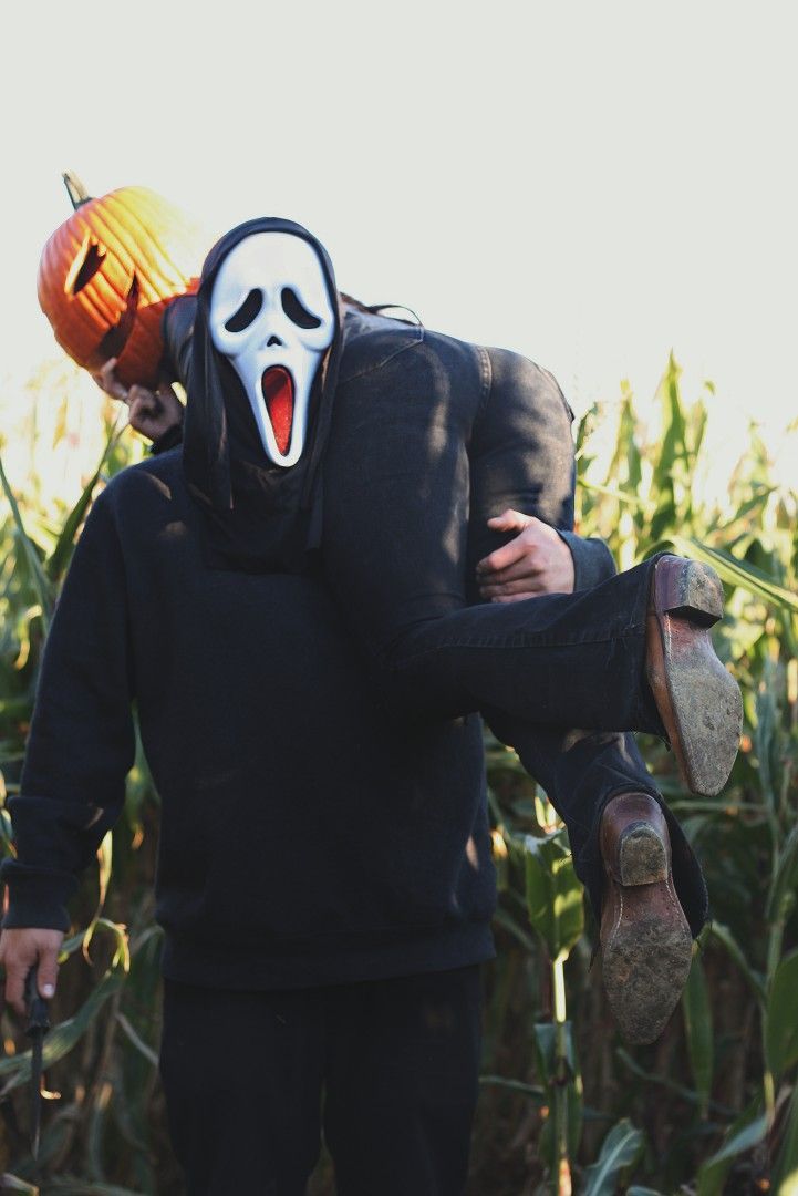 a person wearing a mask and holding a skateboard in front of a corn field