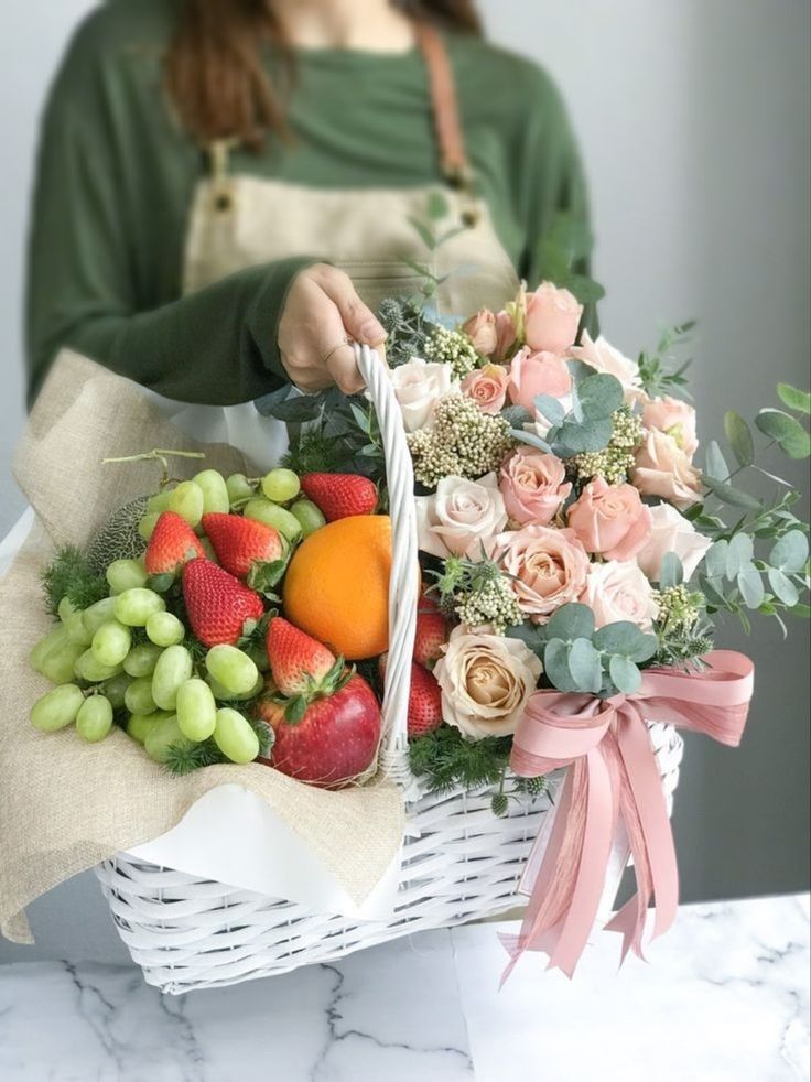 a woman holding a basket full of fresh fruit and flowers on a marble counter top