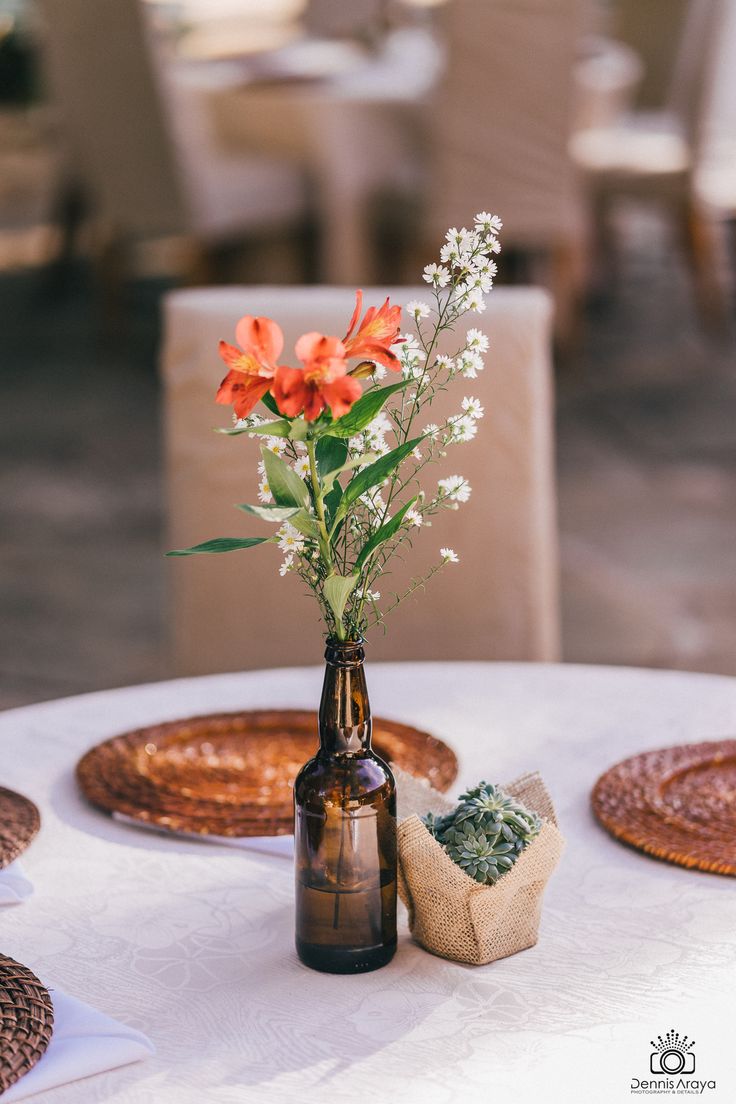 flowers in a brown bottle sitting on top of a table with place settings around it