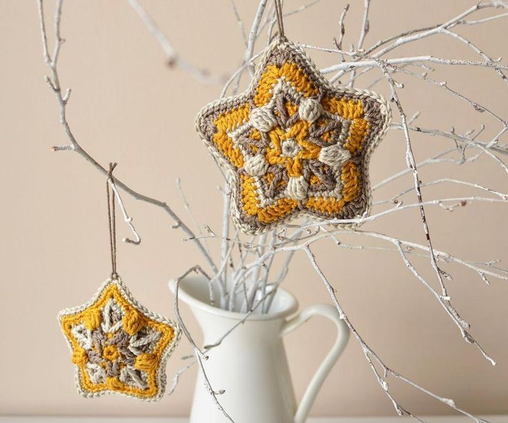 two crocheted snowflakes hanging from branches in a white vase