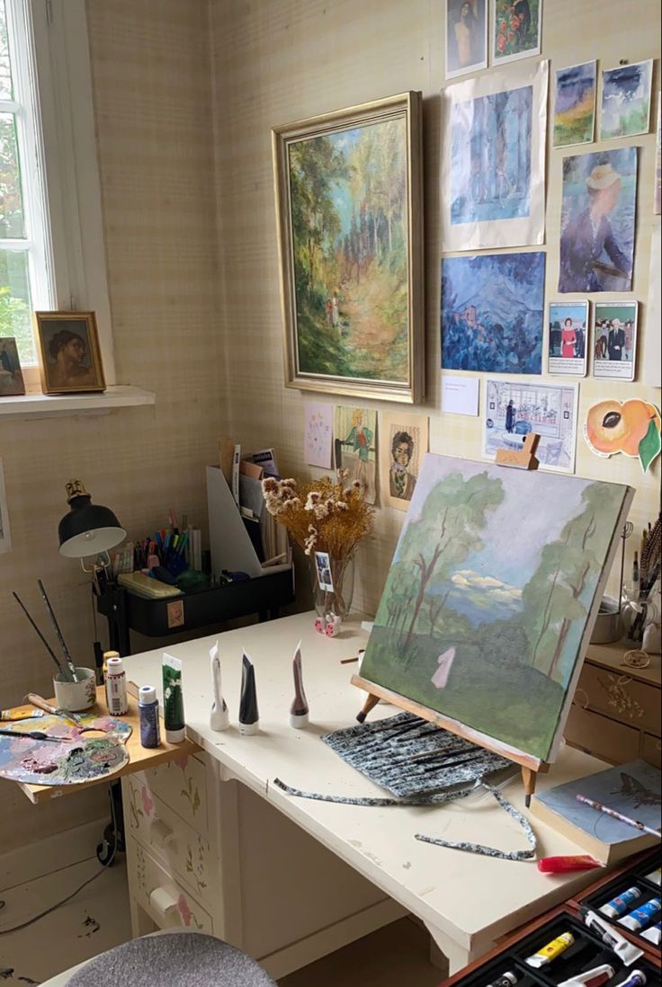 an artist's desk with many paintings on the wall