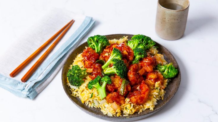 a plate with rice, broccoli and chicken on it next to chopsticks