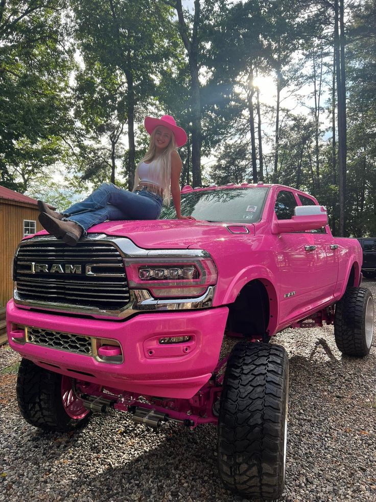 a woman sitting on the hood of a pink truck with large tires and big wheels