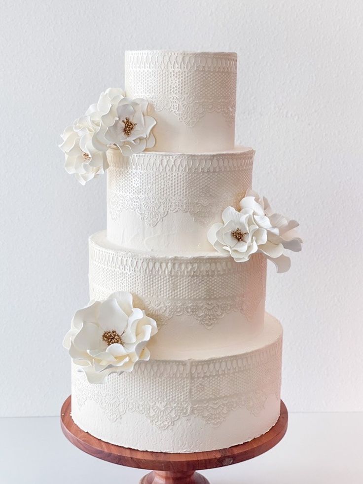 a three tiered wedding cake with white flowers on the top and bottom, sitting on a wooden stand