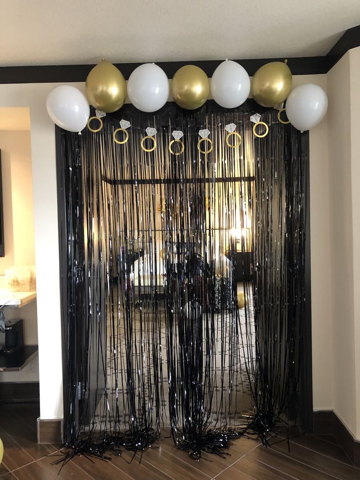 balloons and streamers decorate the entrance to a party with black, gold and white decor