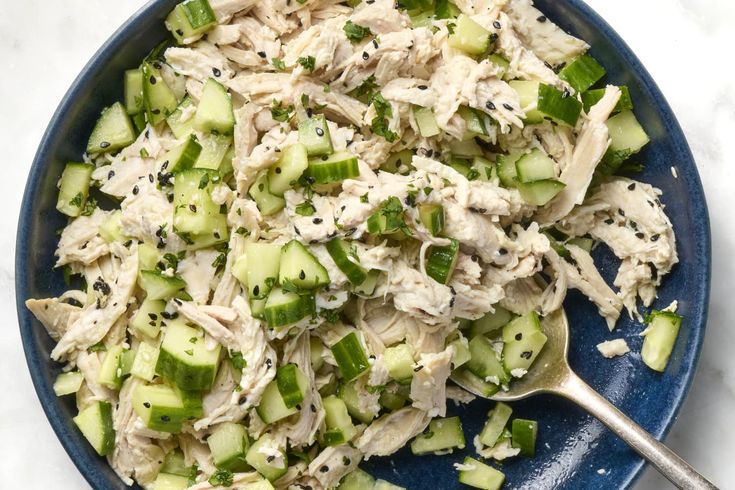 a blue bowl filled with cucumber and chicken salad on top of a white table