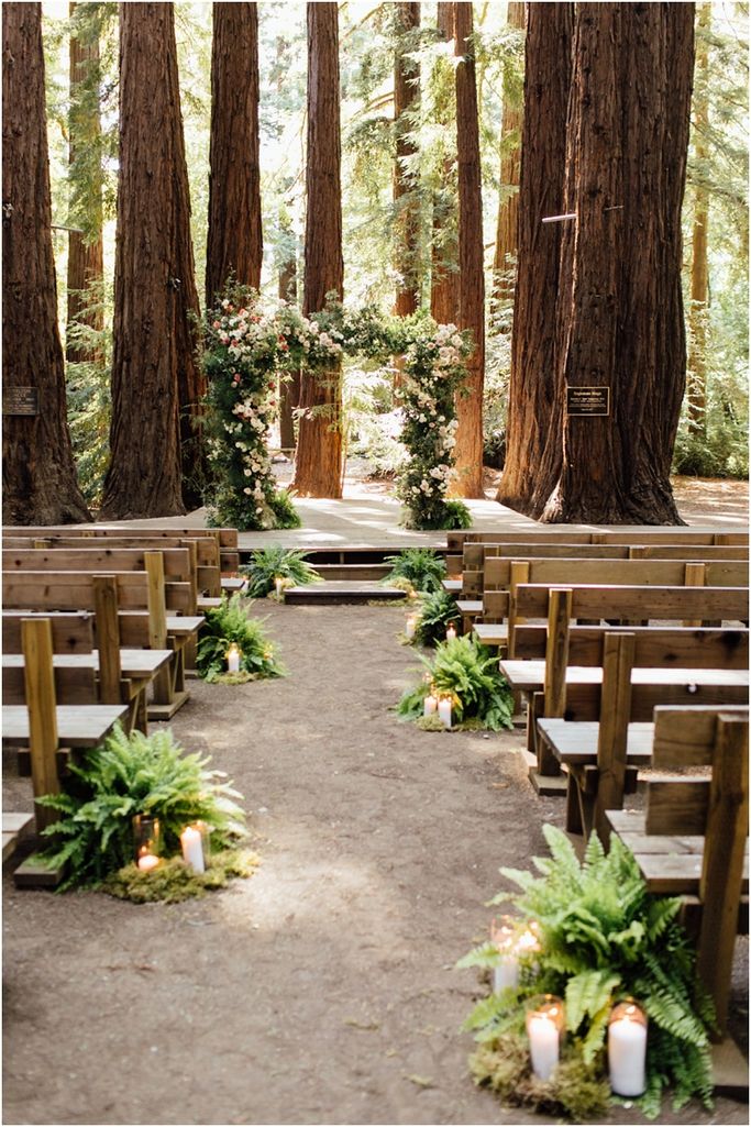 the aisle is lined with greenery and candles for an outdoor ceremony in the woods