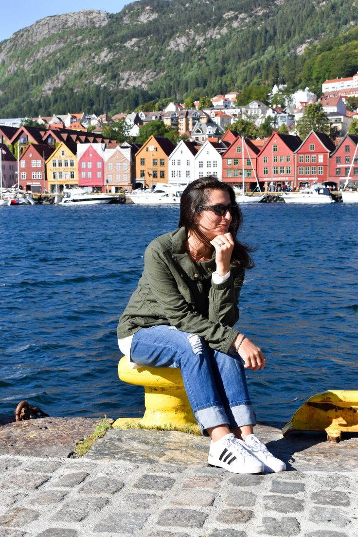 a woman sitting on a yellow bench next to the water with houses in the background