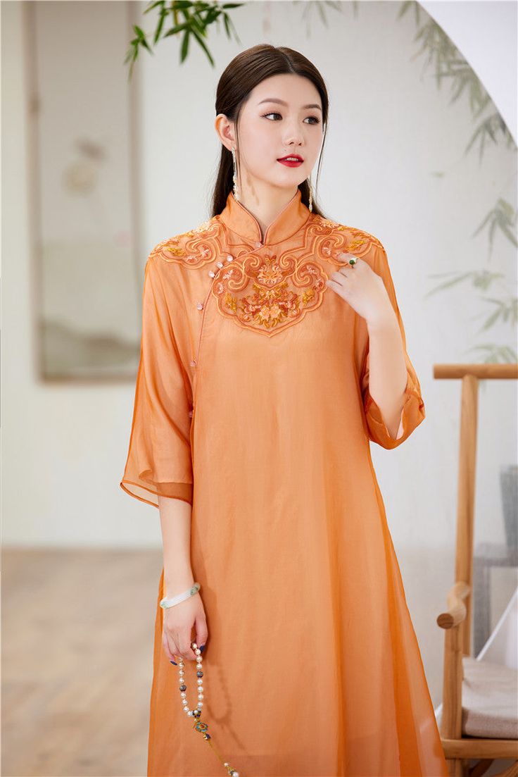 This elegant dress is a modern take on the traditional qipao (cheongsam), featuring a loose fit for comfort and style. The dress is crafted from a lightweight, semi-sheer fabric in a beautiful orange hue, perfect for both casual and formal occasions. Intricate Embroidery: The upper part of the dress is adorned with delicate embroidery, adding a touch of sophistication and artistry. Classic Mandarin Collar: The high, mandarin collar provides a classic and refined look. Asymmetrical Button Closure Traditional Qipao, Qipao Cheongsam, Delicate Embroidery, Qipao Dress, Embroidery Gifts, Wedding Essentials, Intricate Embroidery, Sheer Fabric, Orange Dress