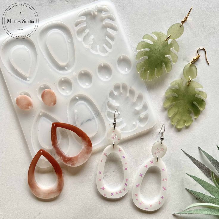 three pairs of earrings sitting next to each other on a white surface with green plants