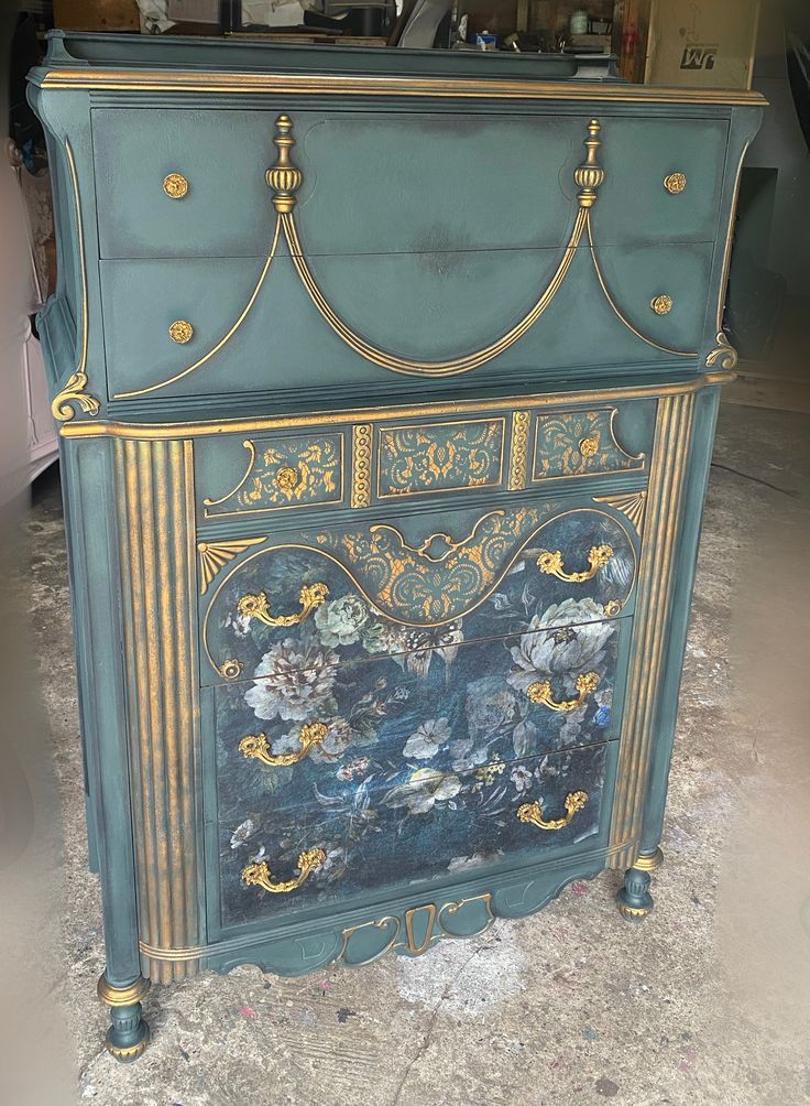 an ornate painted cabinet with gold trimmings and flowers on the front, sitting in a garage