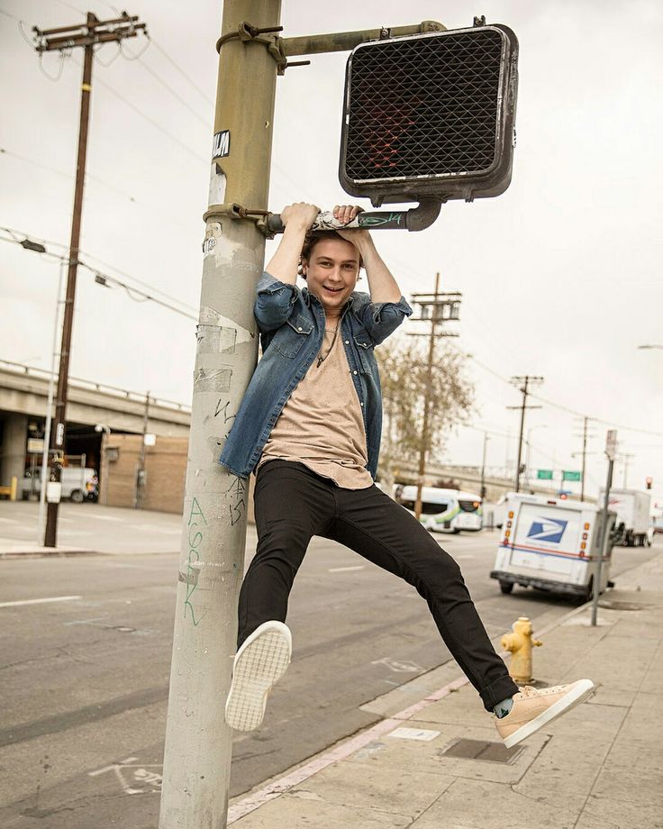 a young man hanging from a street sign on a pole with his hands in the air