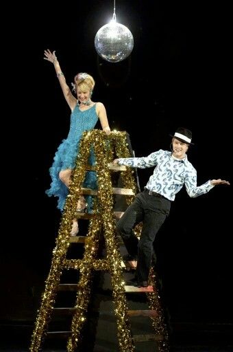 a man and woman are standing on a ladder in front of a disco ball,