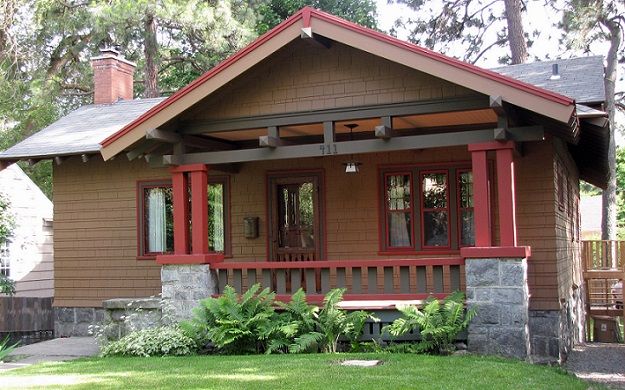 a small brown house with red trim on the front porch and covered porch area, along with lush green grass