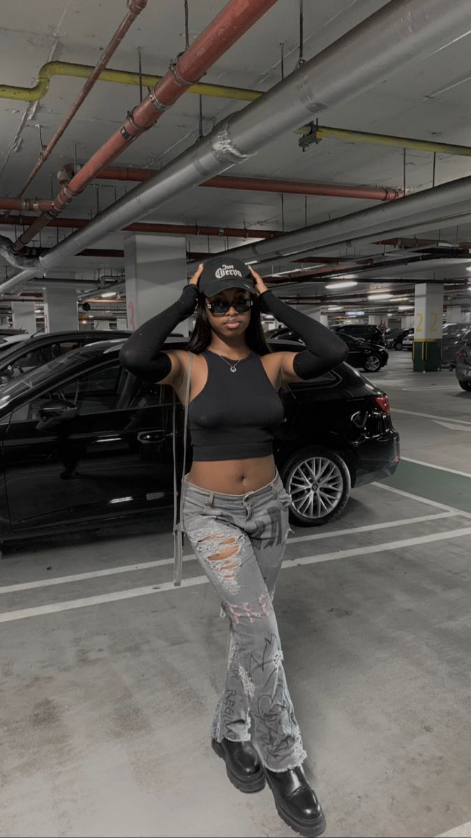 a woman standing in a parking garage with her hands on her head and two cars parked behind her