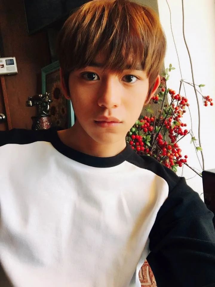 a young man with brown hair wearing a white and black t - shirt in front of flowers