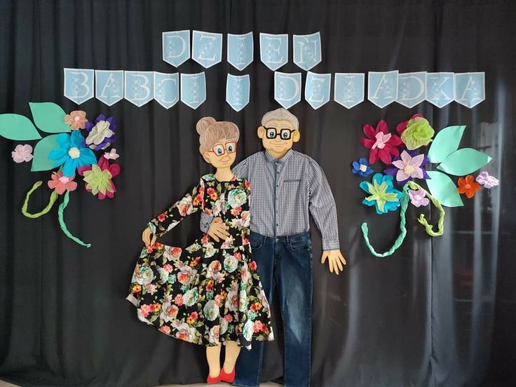 two people standing next to each other in front of a black backdrop with flowers and bunting