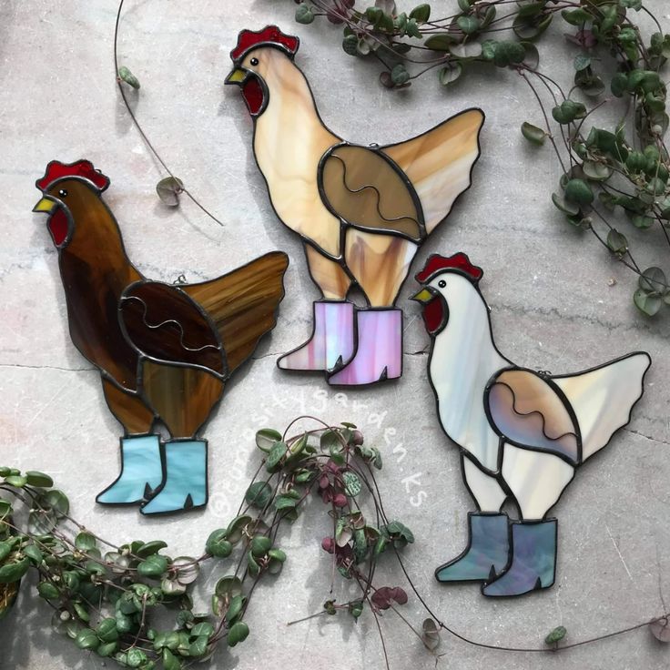 three stained glass chickens standing next to each other on top of a cement ground with green plants