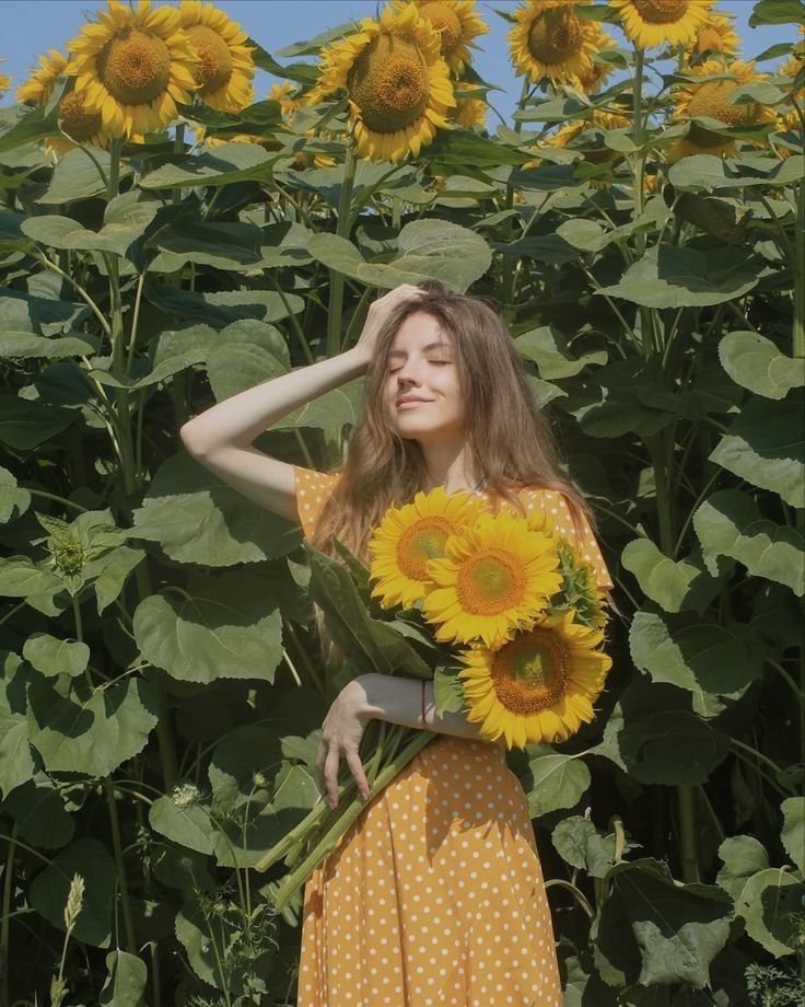 a woman standing in front of a field of sunflowers with her hands on her head