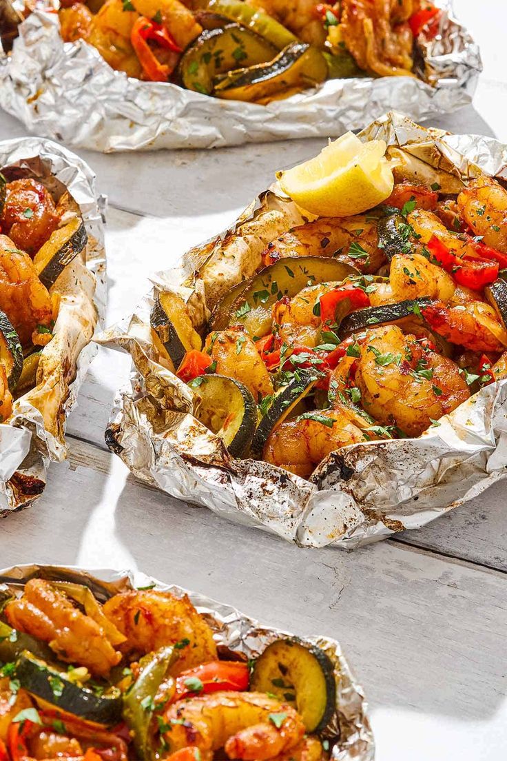 three foil packets filled with different types of food on top of a white wooden table