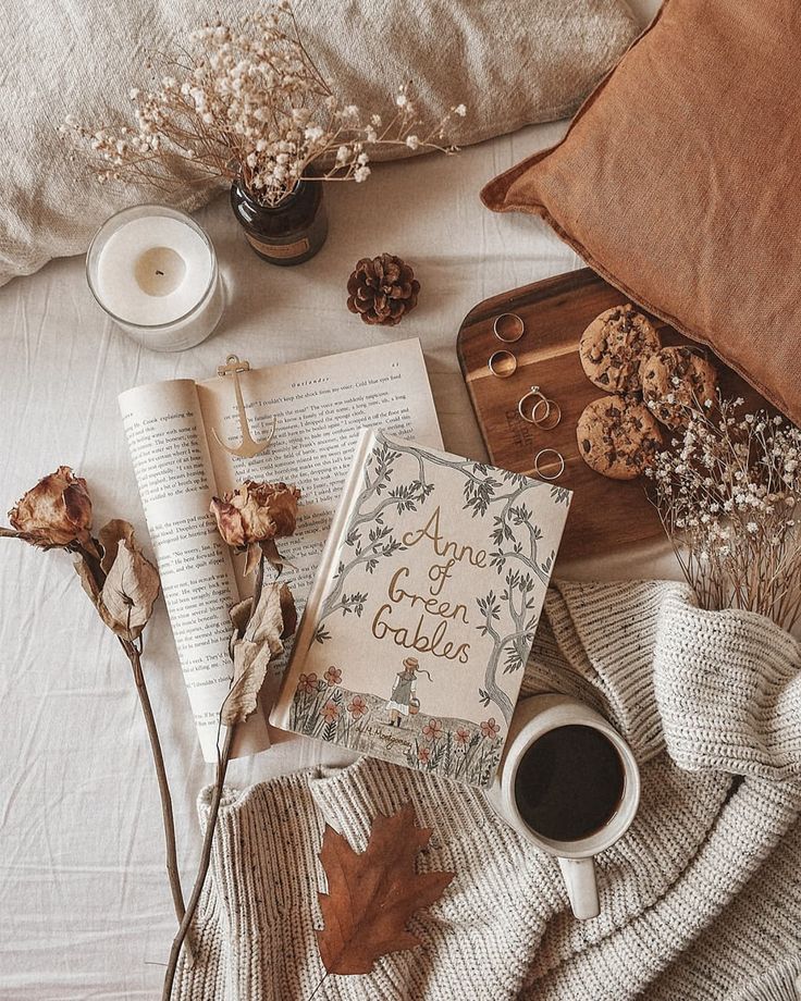 an open book, cup of coffee and other items on a bed with autumn leaves