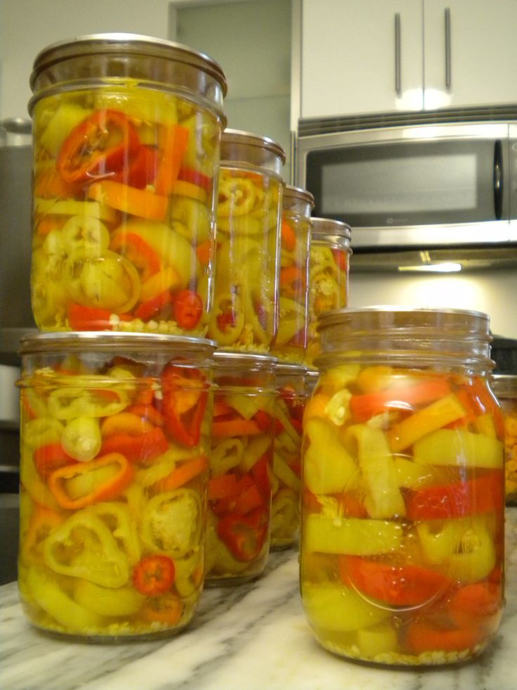 several jars filled with pickled vegetables on a kitchen counter next to a microwave oven