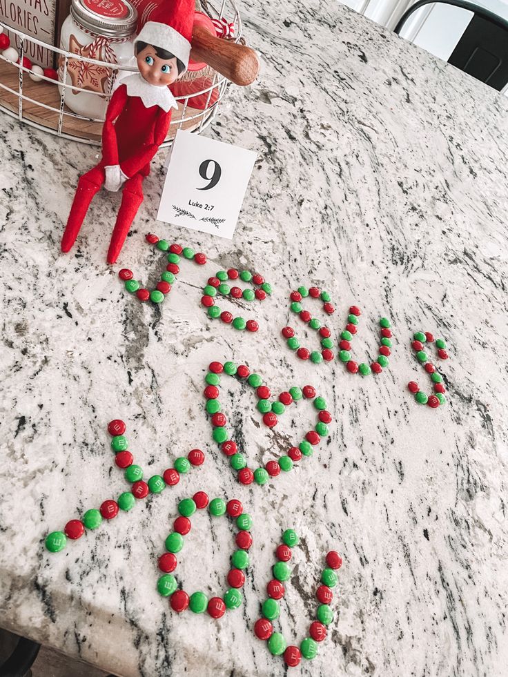 an elf is sitting on the counter next to some candies that spell out love