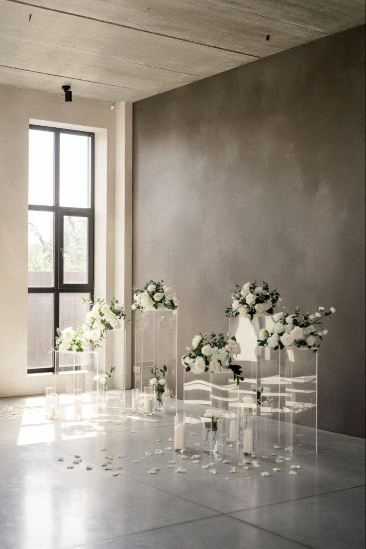 white flowers are arranged in clear vases on the floor next to chairs and windows