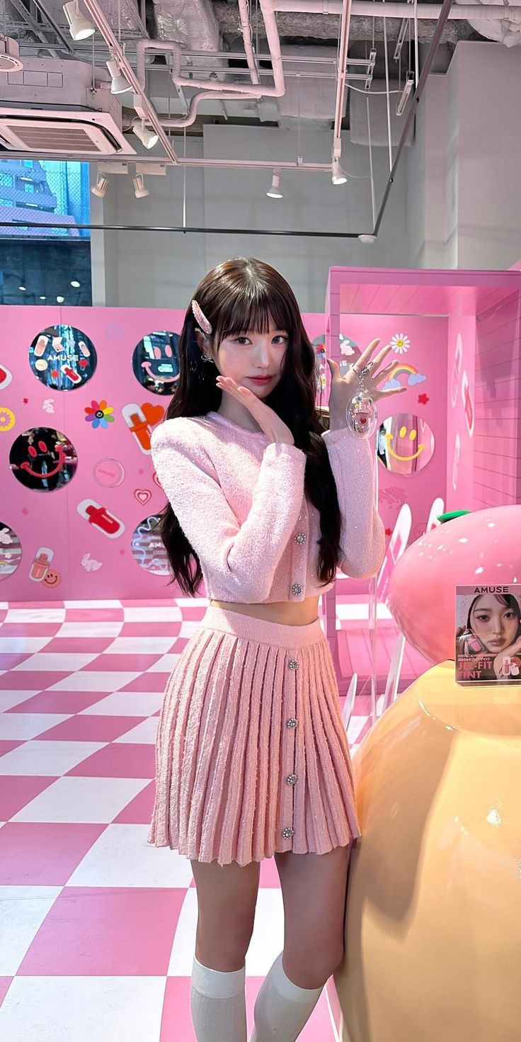 a woman standing in front of a pink and white checkered floor with an odd shaped object behind her