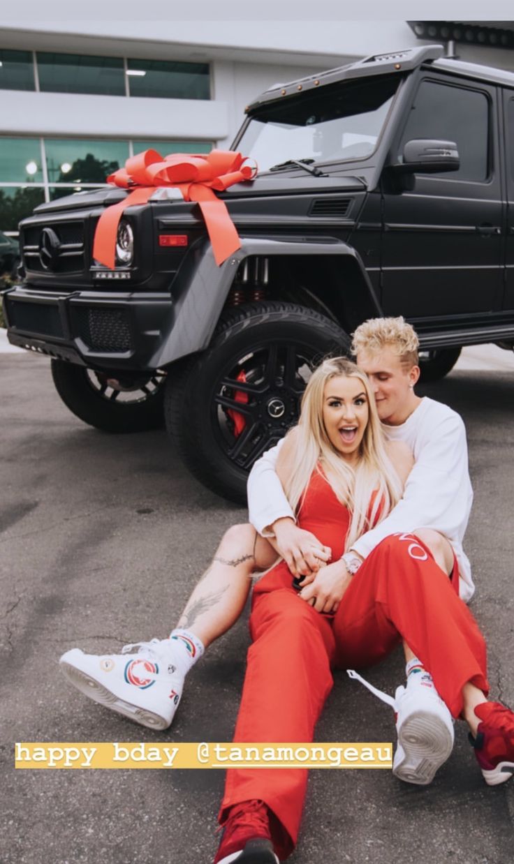 a man and woman sitting on the ground next to a car