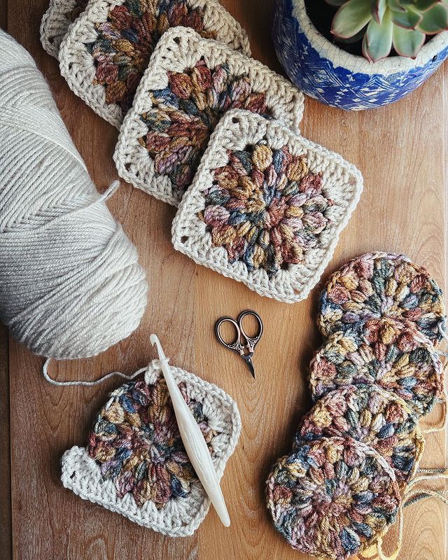 crocheted coasters and yarn on a wooden table with scissors, needles and pot holder