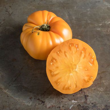 two orange tomatoes sitting on top of a metal counter next to each other, one half eaten