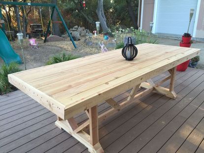 a large wooden table sitting on top of a wooden deck next to a garden area