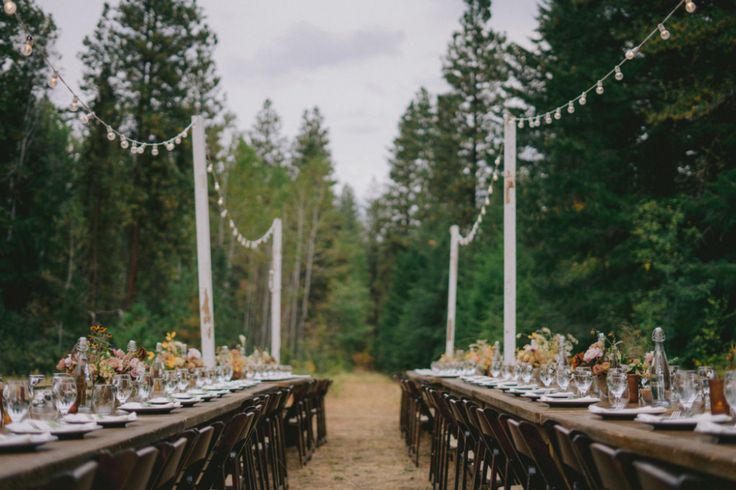 a long table is set with place settings for dinner in the middle of a forest