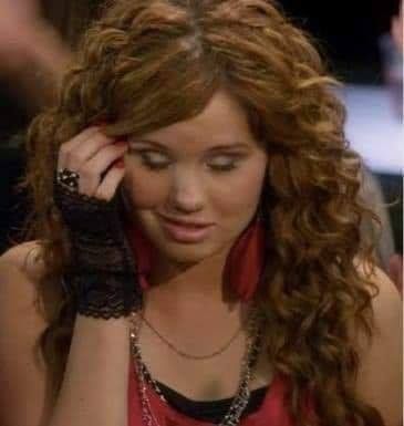 a woman with long curly hair wearing a red shirt and black lace bracelet holding her hand to her head