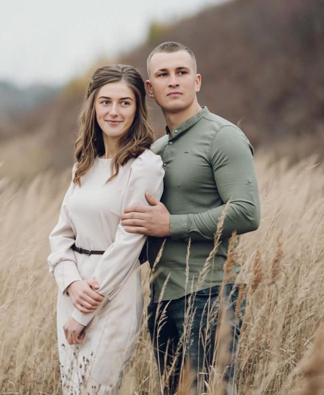 a young man and woman standing in tall grass with their arms wrapped around each other