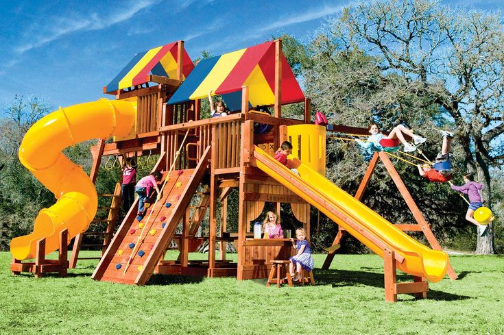 children playing on a wooden play set in the grass with a yellow slide and climbing frame