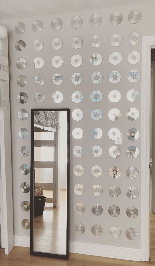 a mirror sitting on top of a wooden floor next to a wall covered in discs