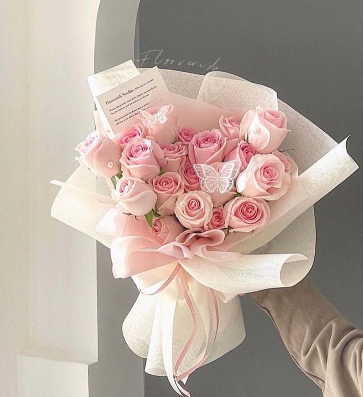 a bouquet of pink roses is being held by a person's hand in front of a door