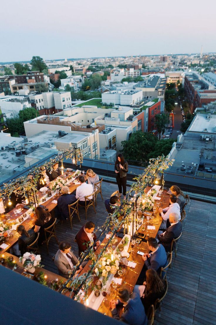 people sitting at tables on top of a roof with cityscape in the background