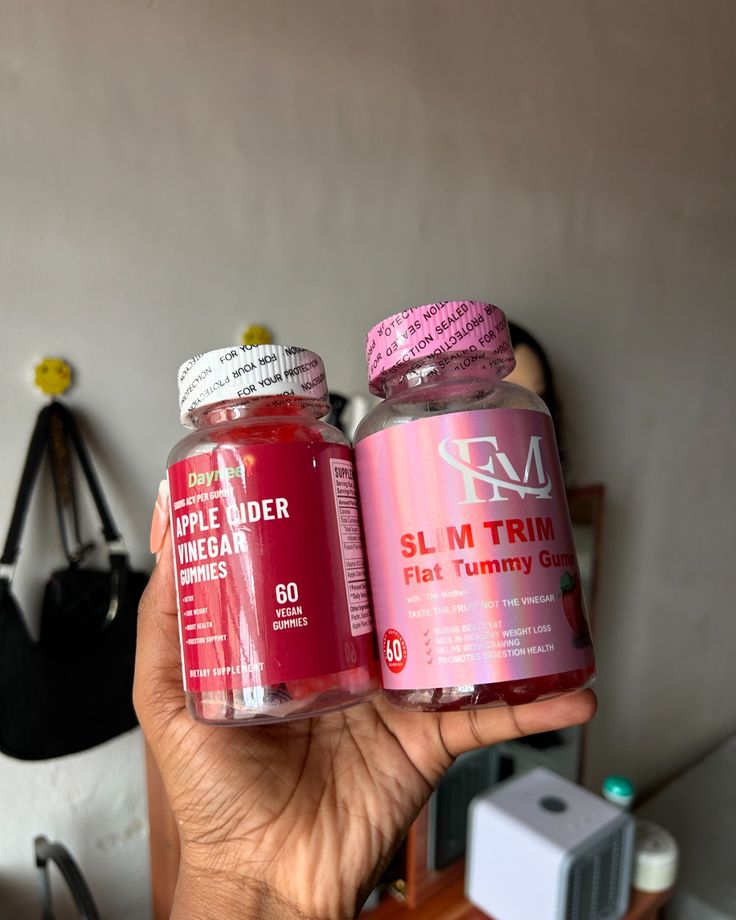 two bottles of vitamin supplements are held in front of a wall with other items on it