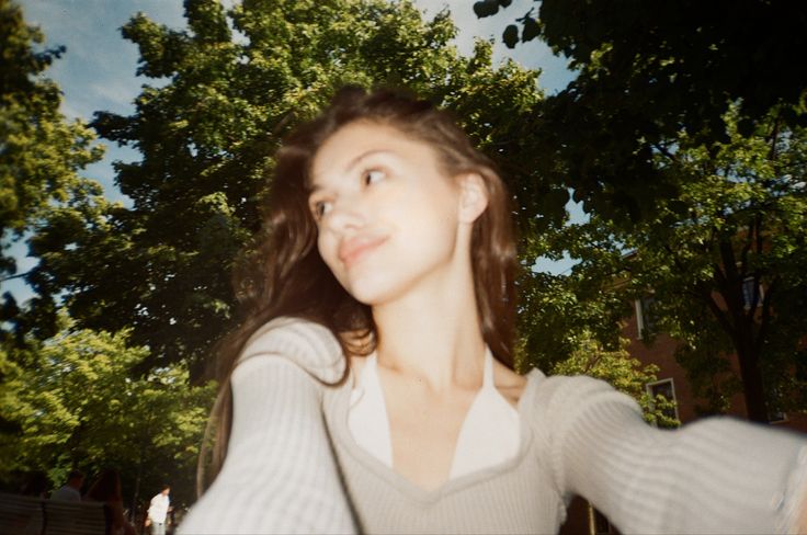 a woman standing in front of trees with her arms out and looking up at the sky