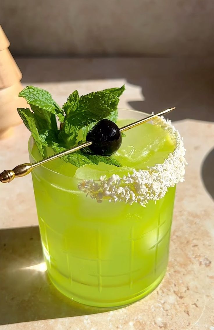 a green drink with some black olives on the top and sprigs in it