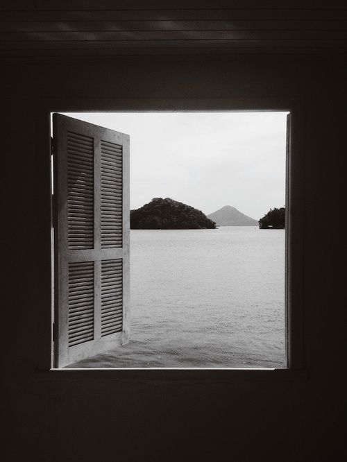 an open window looking out at the water and mountains in the distance, with shutters on either side