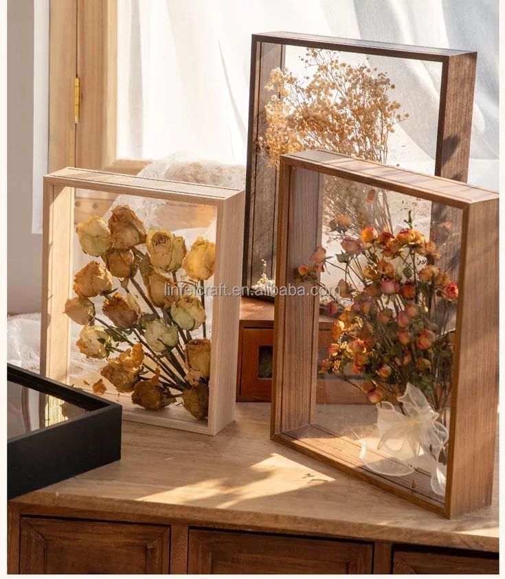 three wooden frames with dried flowers in them on a table next to a glass vase