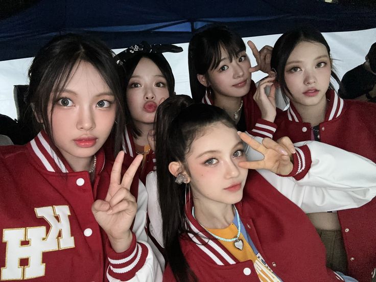 girls in red and white varsity jackets posing for the camera with their fingers raised up