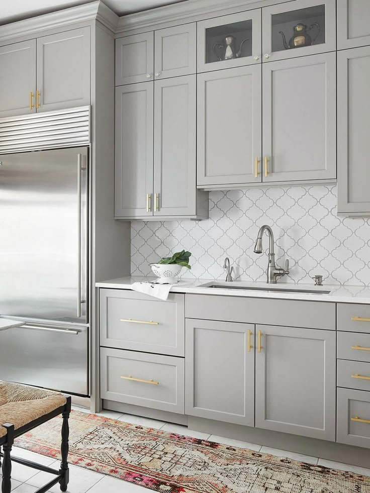 a kitchen with gray cabinets and gold trimmings on the upper cabinetry, along with an area rug